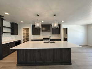 Kitchen featuring tasteful backsplash, light stone counters, an island with sink, a textured ceiling, and recessed lighting