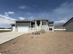 Prairie-style home with stone siding, an attached garage, concrete driveway, and a mountain view