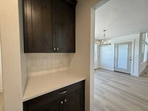 Kitchen with dark brown cabinetry, a textured ceiling, backsplash, light wood-style floors, and light stone countertops