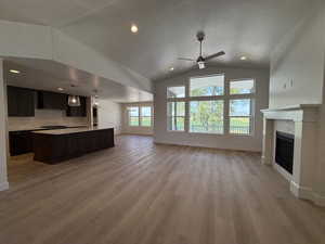 Unfurnished living room with a ceiling fan, lofted ceiling, light wood-style floors, a tile fireplace, and a textured ceiling