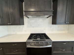 Kitchen with stainless steel gas range, decorative backsplash, dark brown cabinets, and light stone counters