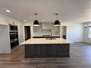 Kitchen with hanging light fixtures, an island with sink, tasteful backsplash, a textured ceiling, and dark wood finished floors