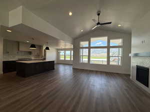 Unfurnished living room with dark wood-style flooring, a tile fireplace, lofted ceiling, a ceiling fan, and a chandelier