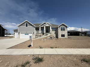 Craftsman-style house featuring stone siding, board and batten siding, an attached garage, driveway, and covered porch