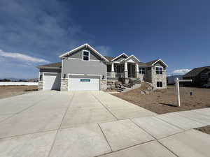 Craftsman house with stone siding, board and batten siding, an attached garage, a porch, and concrete driveway