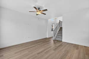 Unfurnished living room with stairs, light wood-style floors, and ceiling fan