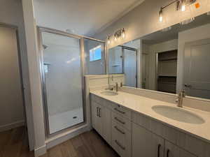 Full bath with a shower stall, dark wood finished floors, a walk in closet, and double vanity