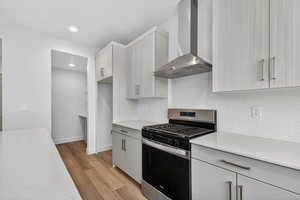 Kitchen with stainless steel gas range, wall chimney exhaust hood, light wood finished floors, modern cabinets, and recessed lighting