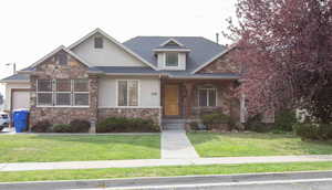 View of front of property with stone siding, a porch, stucco siding, a front yard, and an attached garage