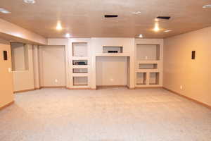 Unfurnished living room featuring built in shelves, light colored carpet, and a textured ceiling
