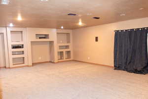 Unfurnished living room with built in features, light colored carpet, and a textured ceiling