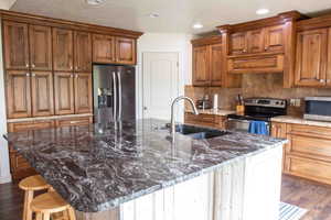 Kitchen featuring dark wood-style floors, brown cabinets, stainless steel appliances, dark stone counters, and recessed lighting