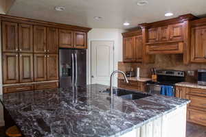 Kitchen featuring appliances with stainless steel finishes, dark stone countertops, brown cabinets, decorative backsplash, and recessed lighting