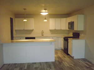 Kitchen with black appliances, white cabinetry, hanging light fixtures, dark wood-type flooring, and a peninsula