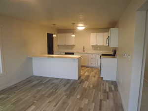 Kitchen with white cabinets, a peninsula, light countertops, light wood-style floors, and decorative light fixtures