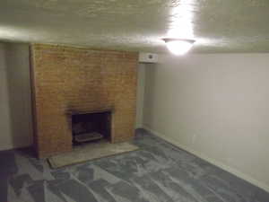 Unfurnished living room with a fireplace, carpet, and a textured ceiling