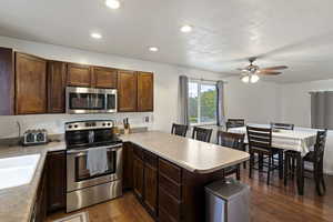 Kitchen with stainless steel appliances, a peninsula, dark wood finished floors, light countertops, and recessed lighting
