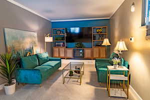 Carpeted living area with crown molding and baseboards