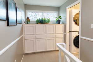 Laundry room featuring stacked washer / dryer and light colored carpet