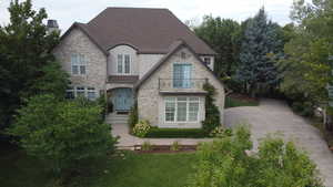 French country inspired facade featuring stone siding, a balcony, stucco siding, and roof with shingles