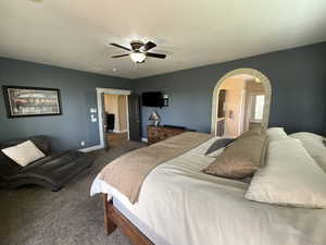 Bedroom with dark carpet, arched walkways, ceiling fan, and ensuite bathroom