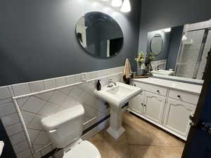 Full bath featuring tile walls, light tile patterned flooring, and wainscoting