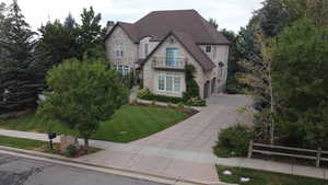 French provincial home featuring stone siding, a garage, concrete driveway, a front lawn, and stucco siding
