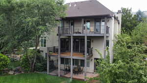 Rear view of property featuring stucco siding, a chimney, roof with shingles, a patio, and a balcony