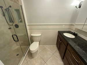 Bathroom with a wainscoted wall, vanity, tile walls, light tile patterned floors, and a shower stall