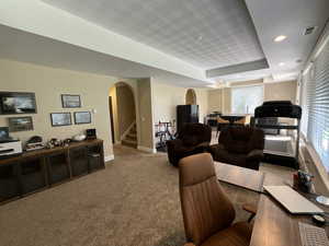 Living area featuring arched walkways, carpet floors, recessed lighting, stairway, and a tray ceiling