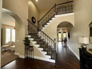 Foyer entrance featuring arched walkways, dark wood-type flooring, a towering ceiling, and stairs