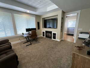 Office area featuring carpet floors, a glass covered fireplace, a tray ceiling, and recessed lighting