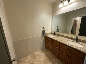 Full bathroom with double vanity, light tile patterned floors, tile walls, and wainscoting