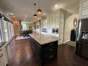 Kitchen with dark cabinets, decorative light fixtures, appliances with stainless steel finishes, light stone countertops, and dark wood-type flooring