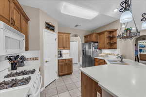 Kitchen featuring arched walkways, white appliances, tasteful backsplash, and brown cabinetry