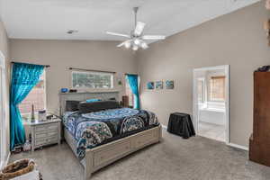 Bedroom with carpet flooring, vaulted ceiling, multiple windows, ceiling fan, and connected bathroom