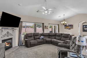 Living area with arched walkways, vaulted ceiling, carpet flooring, a fireplace, and ceiling fan