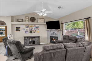 Carpeted living room with lofted ceiling, a tile fireplace, arched walkways, and ceiling fan