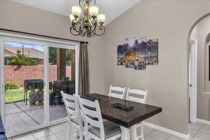 Dining space featuring light tile patterned floors, arched walkways, a chandelier, and vaulted ceiling