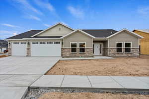 View of front of house with an attached garage, driveway, stone siding, and roof with shingles