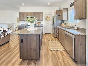 Kitchen with light stone countertops, a center island, light wood-type flooring, appliances with stainless steel finishes, and brown cabinetry
