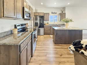 Kitchen with appliances with stainless steel finishes, light stone counters, light wood-type flooring, recessed lighting, and a kitchen island