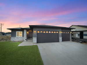 Prairie-style home with stucco siding, driveway, an attached garage, stone siding, and a front yard