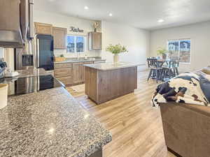 Kitchen featuring light stone countertops, a center island, open floor plan, light wood finished floors, and stainless steel appliances