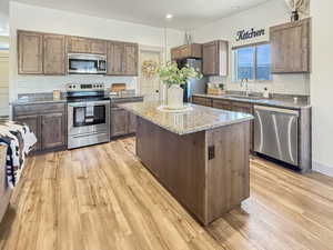 Kitchen featuring appliances with stainless steel finishes, a center island, light stone countertops, light wood-style flooring, and recessed lighting