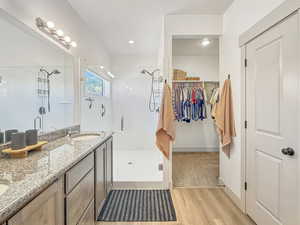 Full bathroom featuring a shower stall, double vanity, a spacious closet, light wood-style floors, and recessed lighting