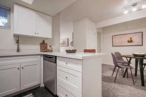 Kitchen with a peninsula, white cabinetry, dishwasher, light stone countertops, and dark carpet