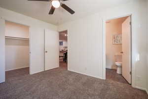 Unfurnished bedroom featuring dark carpet, ensuite bath, ceiling fan, and a closet