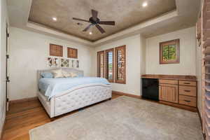 Bedroom with a raised ceiling, light wood-style floors, a ceiling fan, and recessed lighting