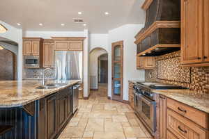 Kitchen featuring arched walkways, tasteful backsplash, stainless steel appliances, light stone countertops, and recessed lighting